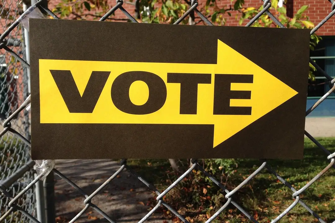 Yellow 'VOTE' sign with an arrow on a chain-link fence, representing voting and decision-making for HOA dissolution.