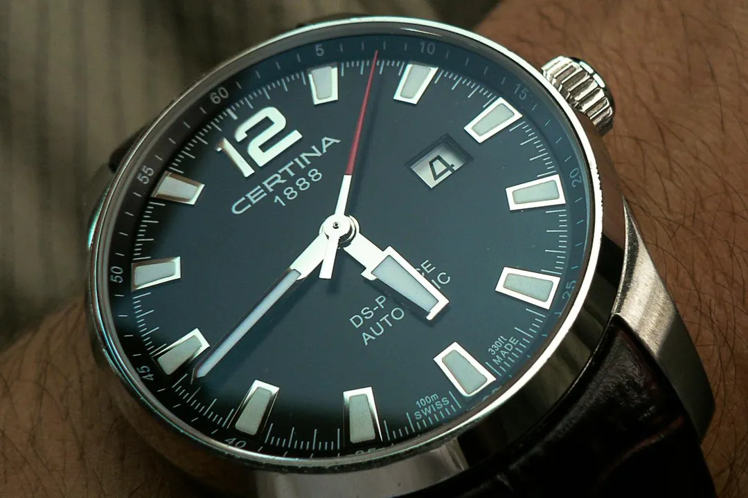 Close-up view of a dark blue dial wristwatch with a silver case and leather strap, showing a date window at the 3 o'clock position.