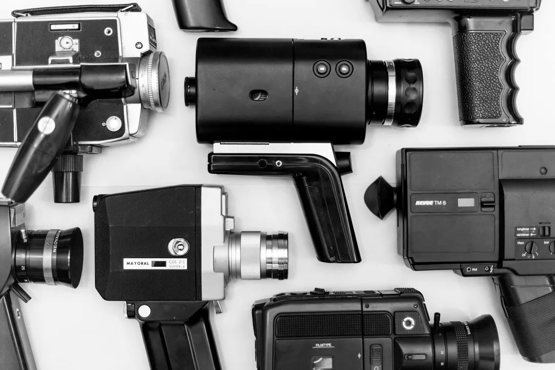 Black-and-white display of various video recording devices, including camcorders and hand-held cameras, arranged on a light surface.