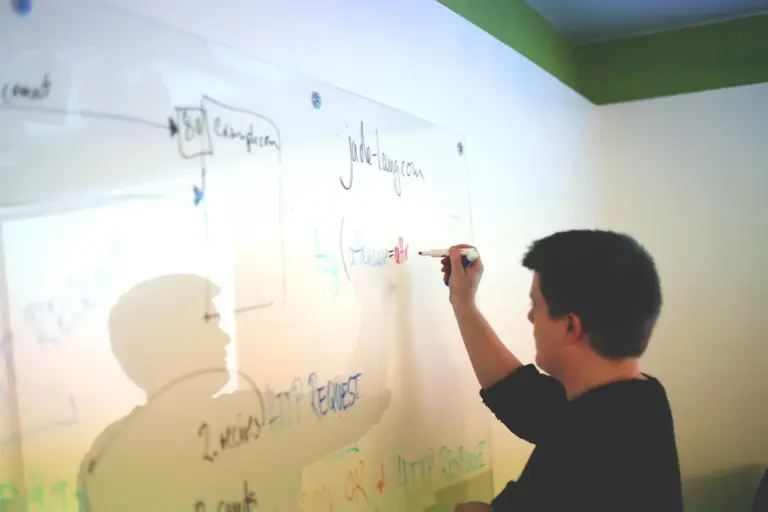 Person writing on a glass whiteboard in an office during a planning session