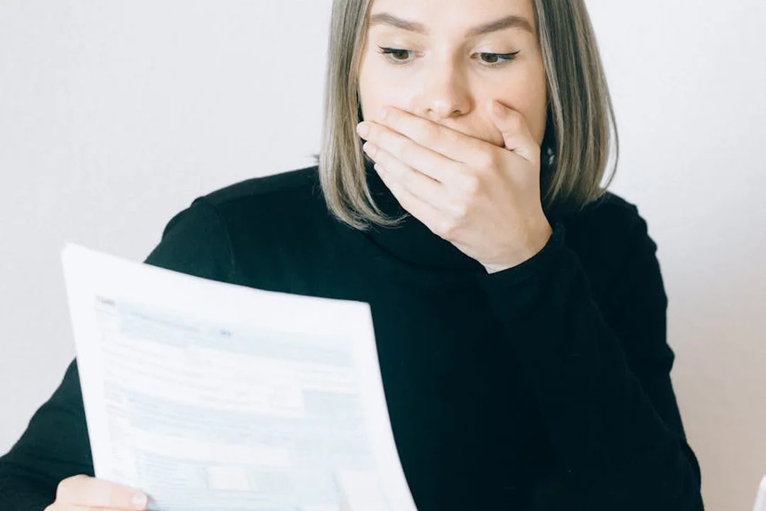 A woman in a black top holds a document in one hand and covers her mouth with the other, appearing concerned while reviewing an HOA bill.