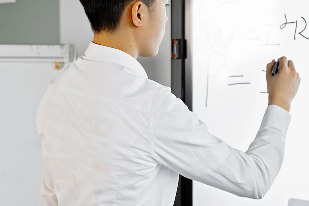 Person in a white shirt writing on a whiteboard with equations in a professional setting.